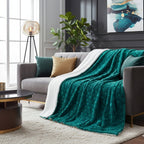Teal blanket draped over a gray sofa in a living room with a plant and artwork.