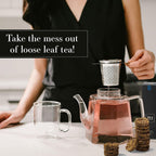 Person using a tea infuser with loose leaf tea on a table, with text 'Take the mess out of loose leaf tea!'.