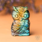 Crystal owl figurine with labradorite patterns on a warm-toned background